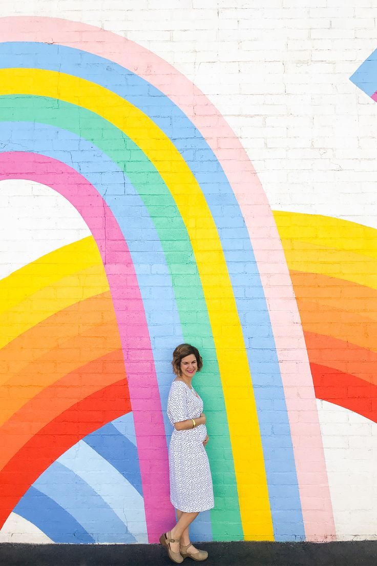 a woman standing in front of a rainbow painted wall