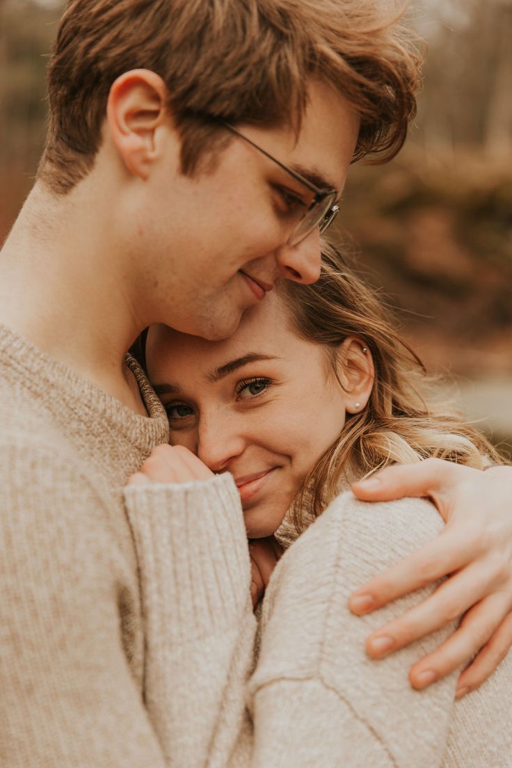 a man and woman hugging each other in front of some trees with their eyes closed