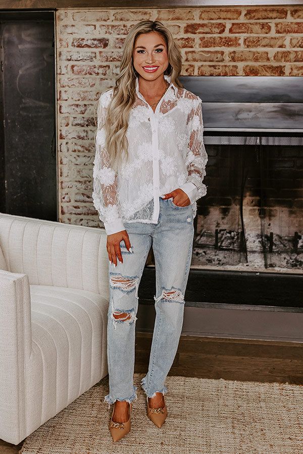 a woman standing in front of a fire place wearing ripped jeans and a white shirt