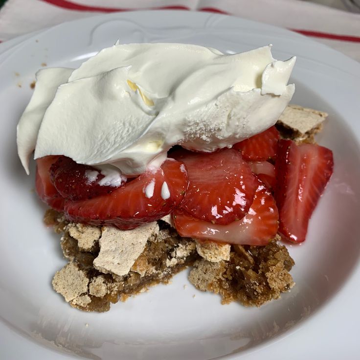 a dessert with strawberries and whipped cream is on a white plate, ready to be eaten