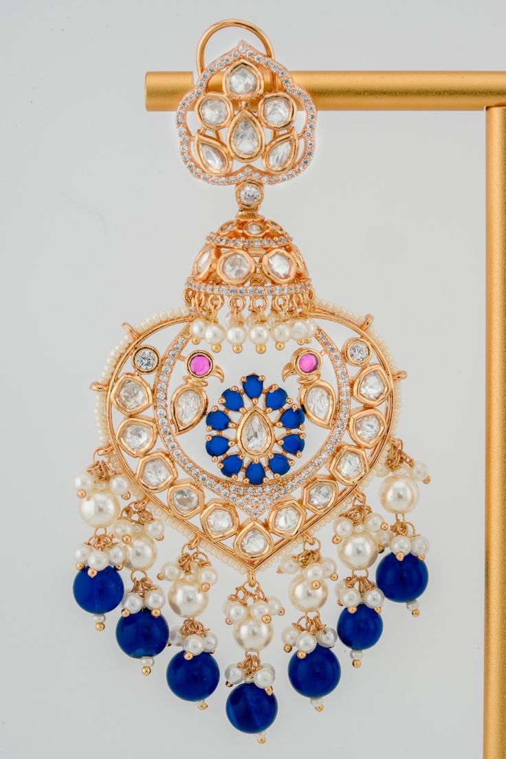 An opulent beauty, BAALI's Afreen Chandbali is no ordinary statement earring. This artisan-made modern kundan chandbali is a 21K gold plated earring and features an enchanting flower and peacock centerpiece handcrafted with colorful gemstones. It is perfected with lustrous colored pearl drop accents and dazzling kundan stones that sparkle in every environment. The ethereal beauty of this unique South Asian jewelry piece will captivate crowds at every special occasion. Materials: 21K gold plating on brass, kundan stones, pearls Dimensions (L x W): 4.0 x 2.25 inches Weight: 31g (per chandbali) Blue Drop Earrings For Bridal Festive Occasions, Blue Bridal Drop Earrings For Festive Occasions, Blue Kundan Earrings Hand Set, Hand-set Blue Bollywood Earrings, Elegant Blue Chandbalis For Celebrations, Blue Chandbali Hand Set Earrings, Blue Chandbali Danglers For Celebration, Traditional Hand Set Blue Bridal Earrings, Traditional Blue Chandelier Earrings For Celebration