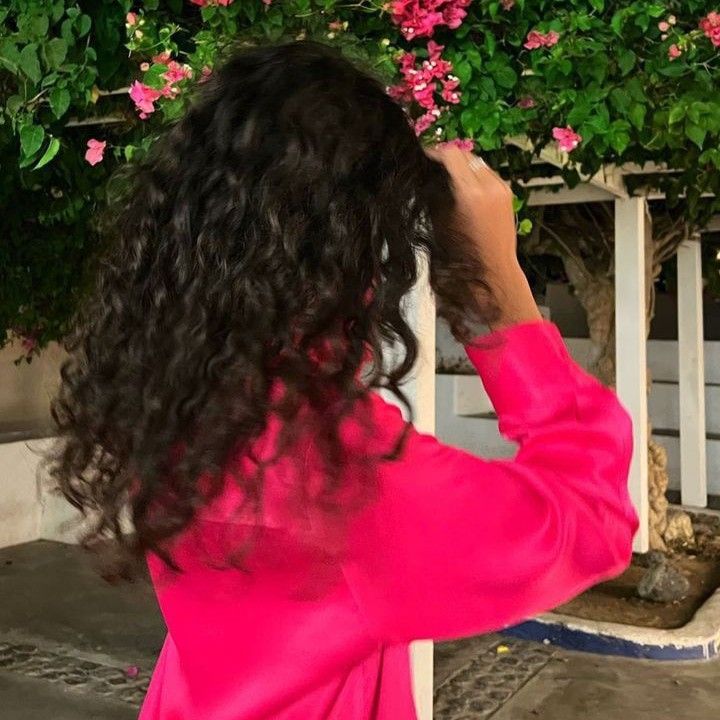 a woman in a pink dress is looking at flowers on the wall and she has her hands behind her head