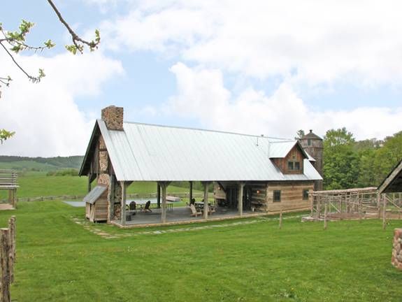 an old log cabin sits in the middle of a grassy field with picnic tables and benches