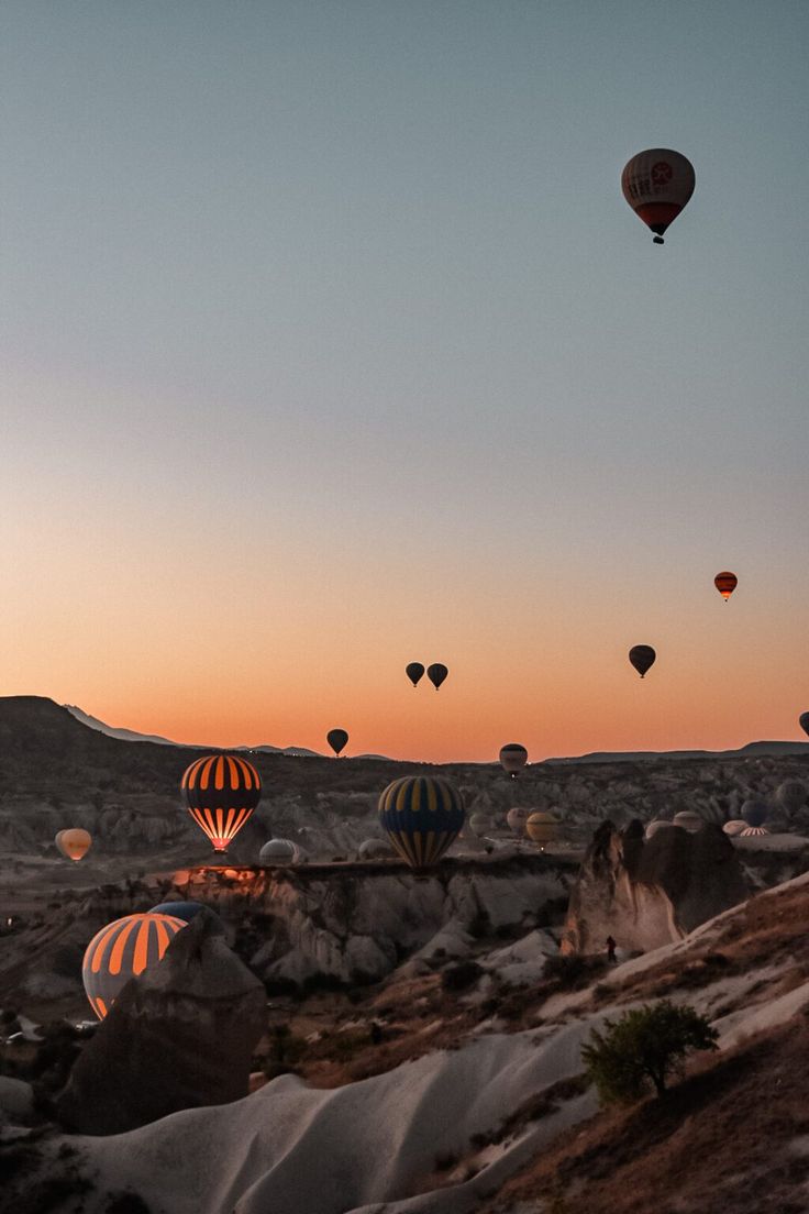 many hot air balloons are flying in the sky above some rocks and sand at sunset