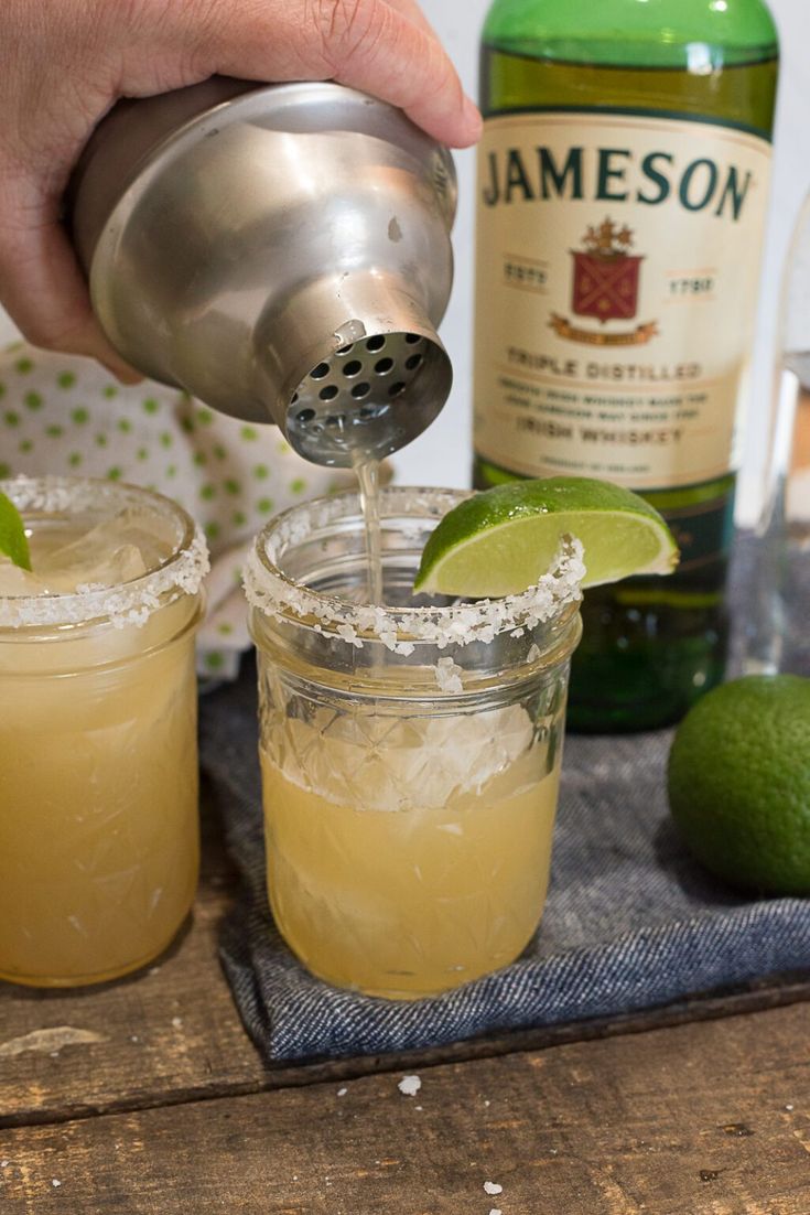 a person pours a drink into two glasses with lime wedges on the side