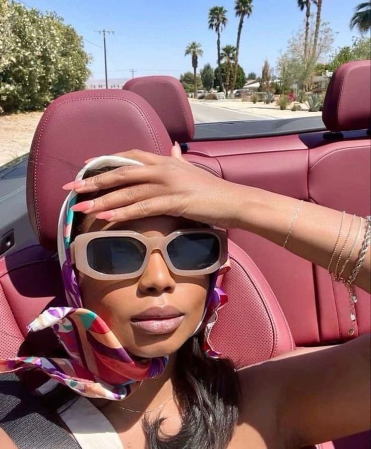 a woman sitting in the back seat of a car wearing sunglasses and a scarf around her head