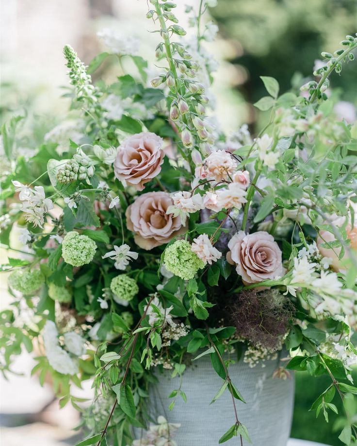 a vase filled with lots of flowers sitting on top of a white table covered in greenery