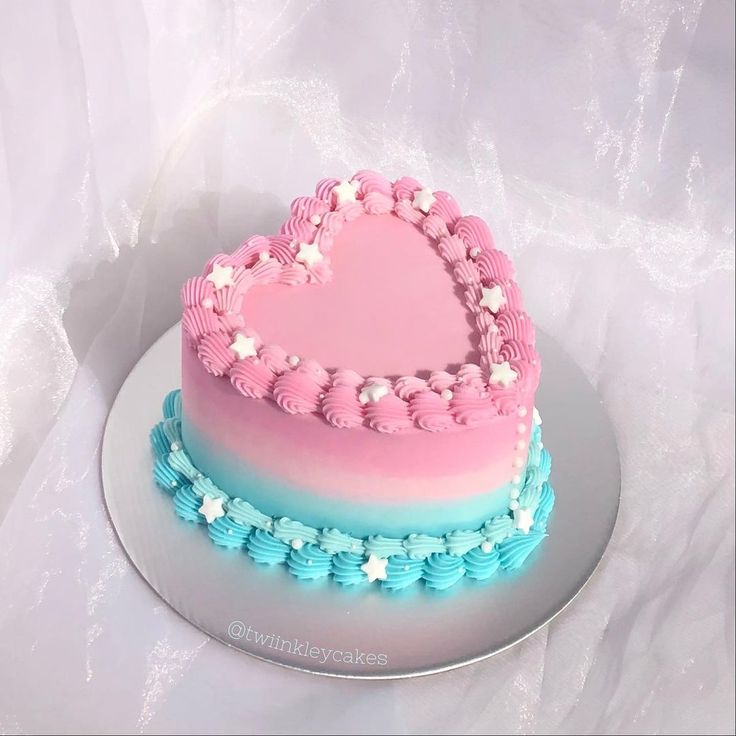 a heart shaped cake with blue and pink frosting on a white tablecloth background