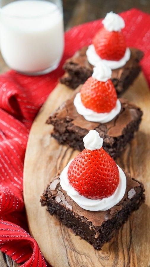 chocolate brownies with strawberries and whipped cream on top are sitting on a wooden platter