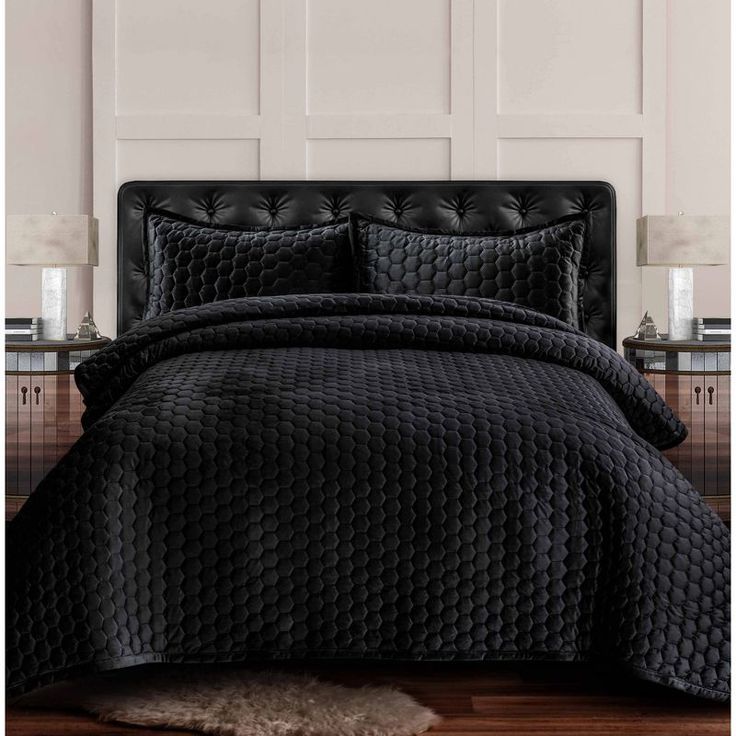 a bed with black comforter and pillows on top of the headboard in front of a white paneled wall