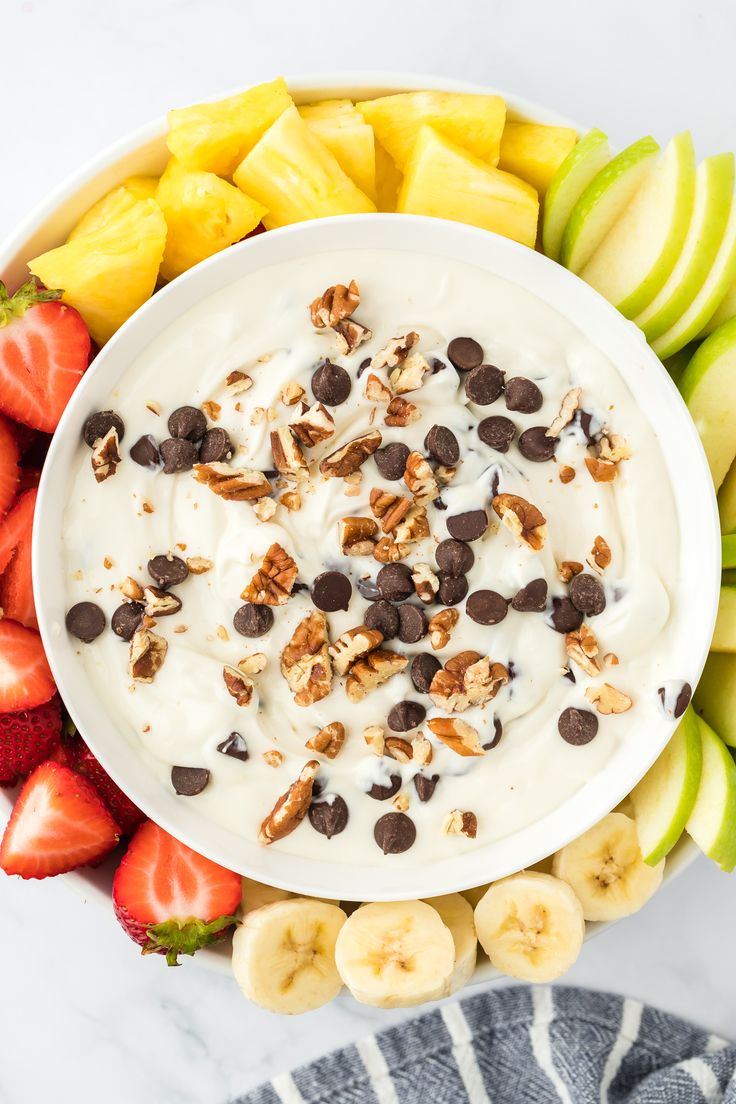 a bowl of yogurt surrounded by sliced bananas, strawberries and chocolate chips