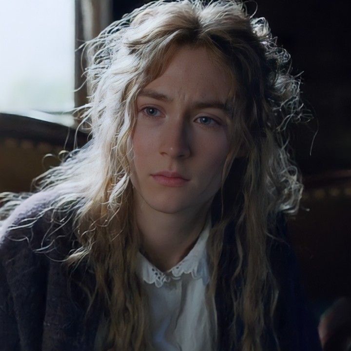 a woman with long hair sitting in front of a window and looking at the camera