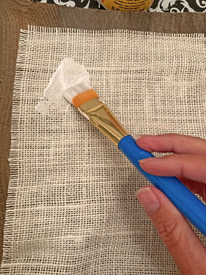 a person holding a blue and yellow brush on top of a piece of cloth next to a bottle