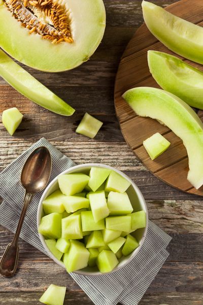 sliced green apples in a bowl on a wooden table with spoons and cutting board