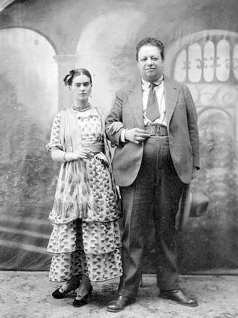 an old black and white photo of a man and woman standing in front of a wall