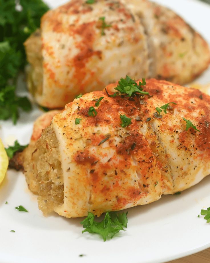 two pieces of chicken on a white plate with parsley and lemon wedges next to it