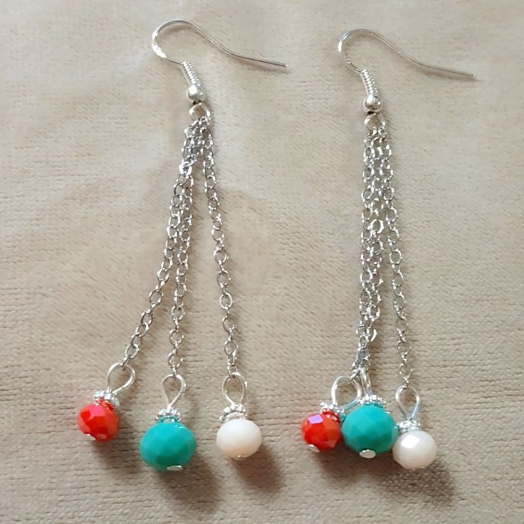 two pairs of dangling earrings with beads and chains on top of a tablecloth covered surface