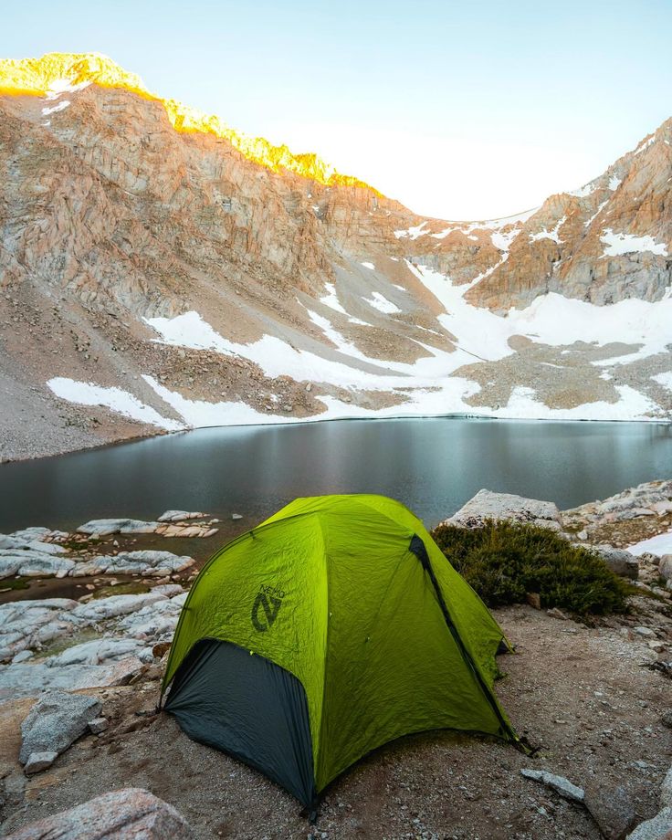 a tent pitched up on the side of a mountain with a lake in the background