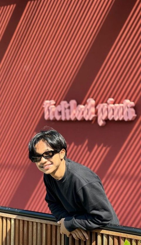 a man wearing sunglasses leaning on a wooden fence with his head resting on the railing