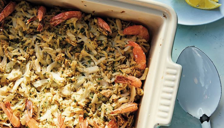 a casserole dish with shrimp, rice and lemon wedges on the side