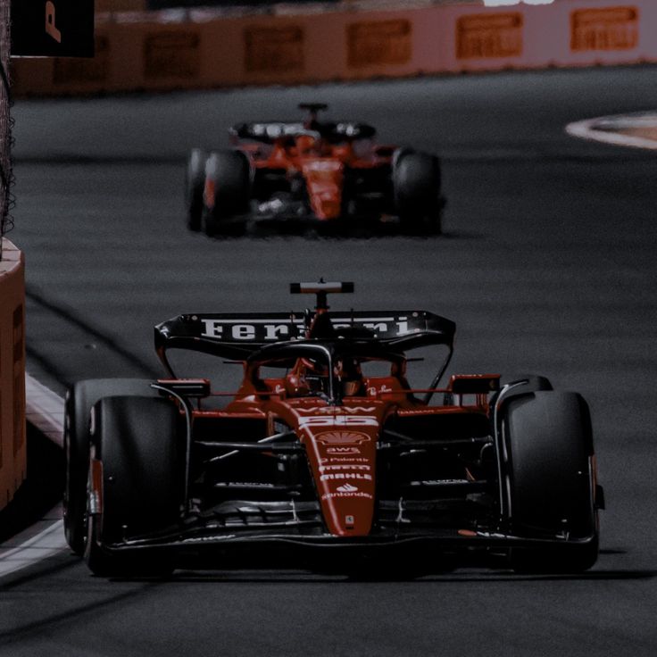 two red race cars racing on a track with one driving behind the other in motion