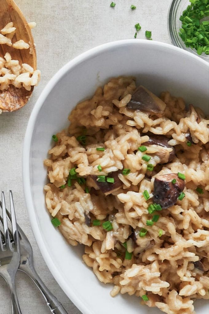 a white bowl filled with rice and mushrooms next to silverware on top of a table