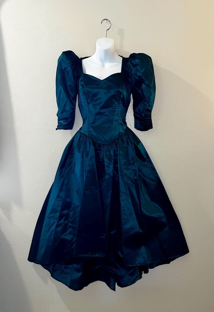 This vintage 80s party/prom dress is a stunning piece that will make you stand out at any party or special occasion. The dress is made of high-quality dark green satin stiff material. This dress is perfect for wearing as is to a retro 1980s gala or would be a great start to a gothic black Halloween costume. This has a sweetheart neckline. The bodice is fitted and has 3/4 ruched sleeves that are puffed at the shoulders bottom of sleeve is fitted, zips at back waist with a peekaboo Center, bow at the back of the shoulders. and has a super full midi Hilo skirt. No size tag, I believe it should fit a modern small size, (please note this has been altered and I believe you could get another inch if taken out at the bustline & waist) but please refer to the actual measurements below for a proper Black Halloween Costume, 1980s Prom Dress, Prom Dress Green, 1980s Prom, Black Halloween Costumes, Wedding Costume, Wedding Costumes, 80s Party, Green Prom Dress