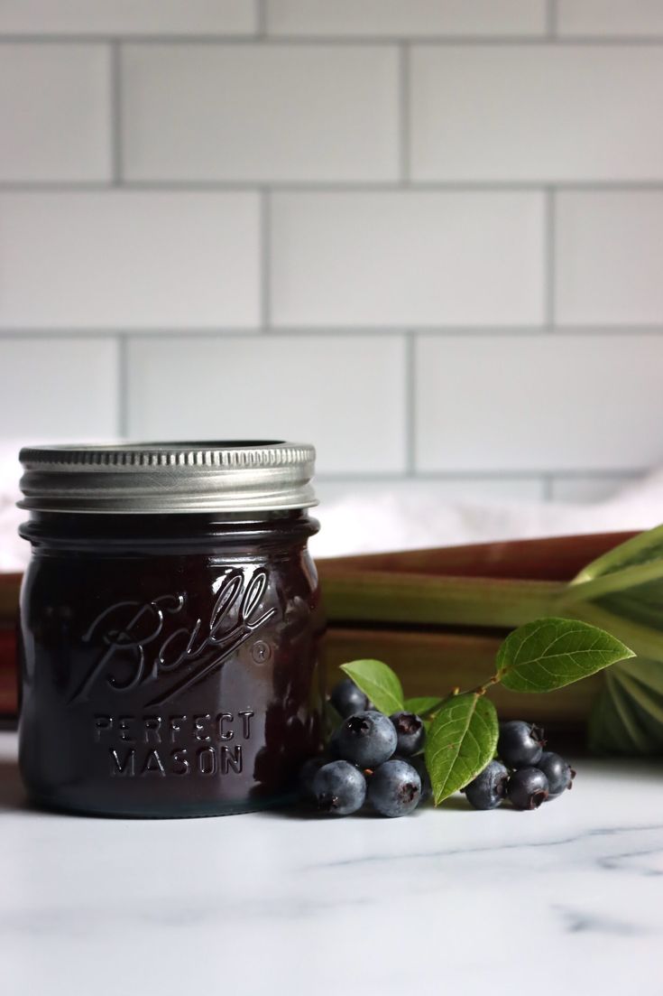 a glass jar filled with blueberries sitting on top of a counter next to green leaves