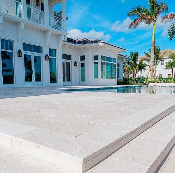 an empty pool in front of a large white house with palm trees on the other side