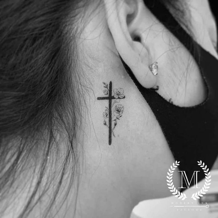 a woman's neck with a cross tattoo on her left side behind the ear