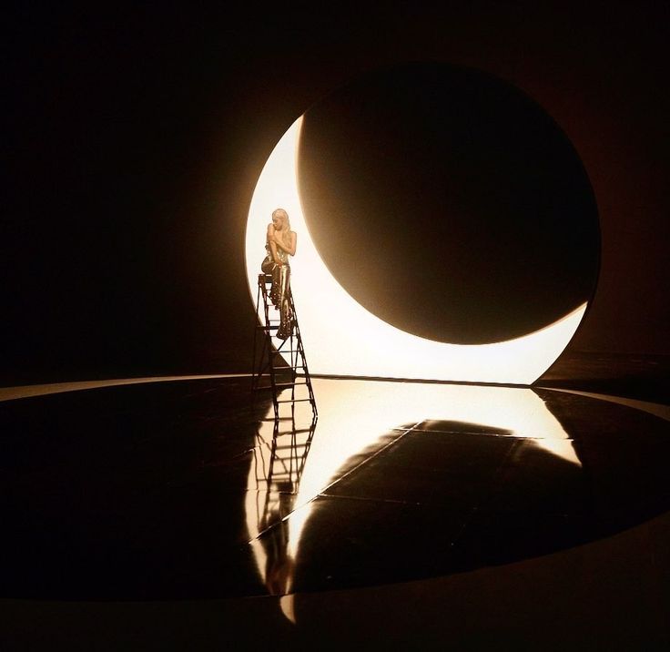 a man on a ladder standing in front of a large object with the moon behind him