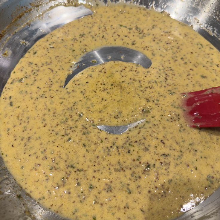 a red spatula in a metal pan filled with yellow liquid and other food items