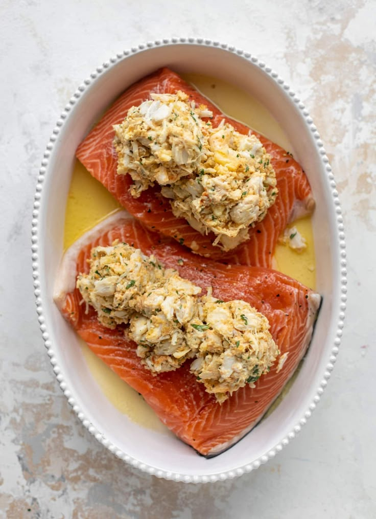 two raw salmon fillets in a white bowl with mustard sauce and herbs on top