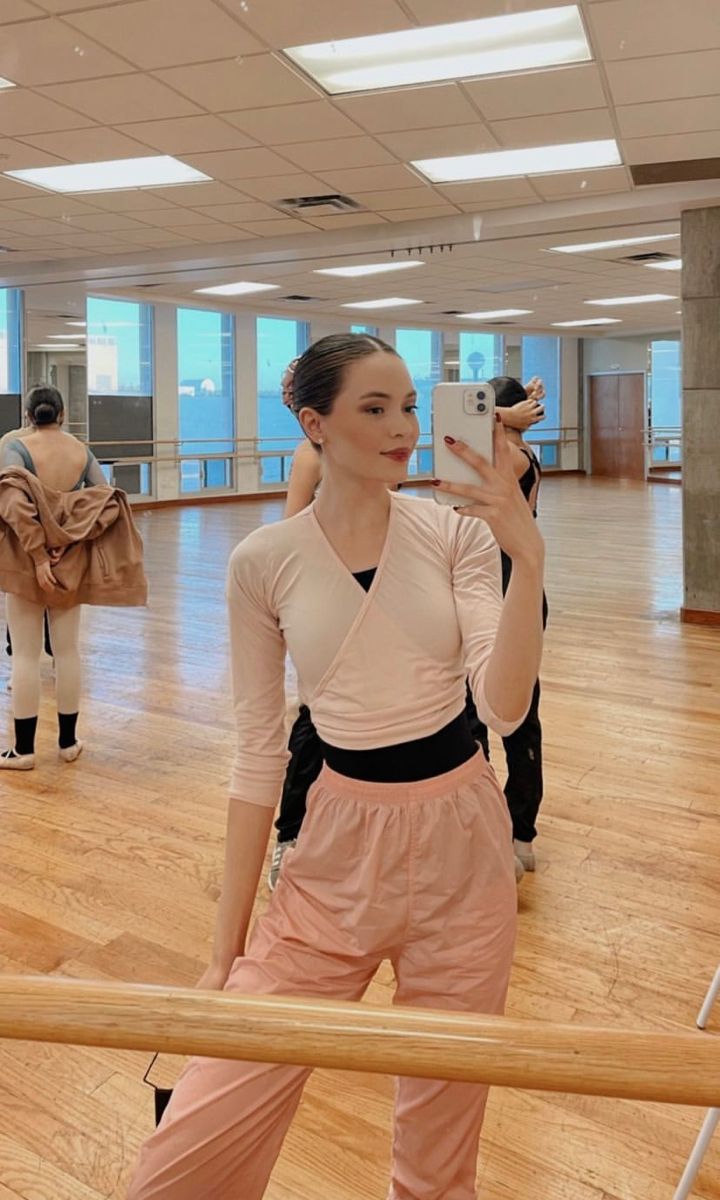 a woman taking a selfie in an empty dance studio with other dancers behind her