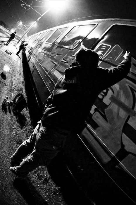 a man leaning against the side of a car at night with his arms in the air