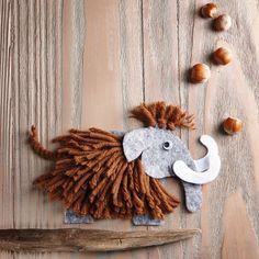 an elephant made out of felt sitting on top of a wooden table next to acorns