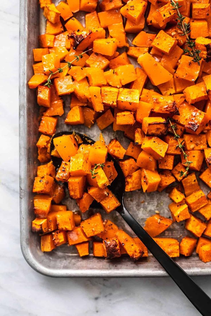 roasted sweet potatoes on a baking sheet with a serving spoon