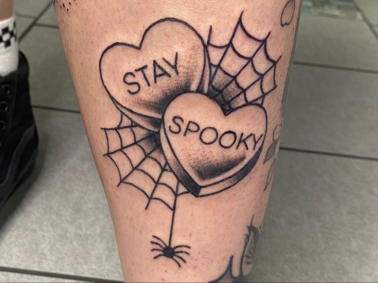 a tattoo on the leg of a person with two hearts and spider webs, saying stay spook