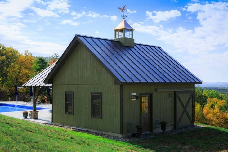 a small green building with a steeple on top and a pool in the background