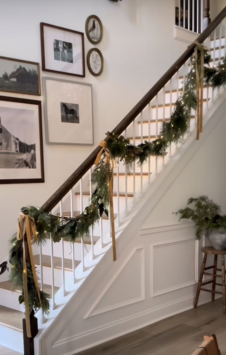 the stairs are decorated with christmas garlands and pine cones for holiday decor, along with pictures on the wall