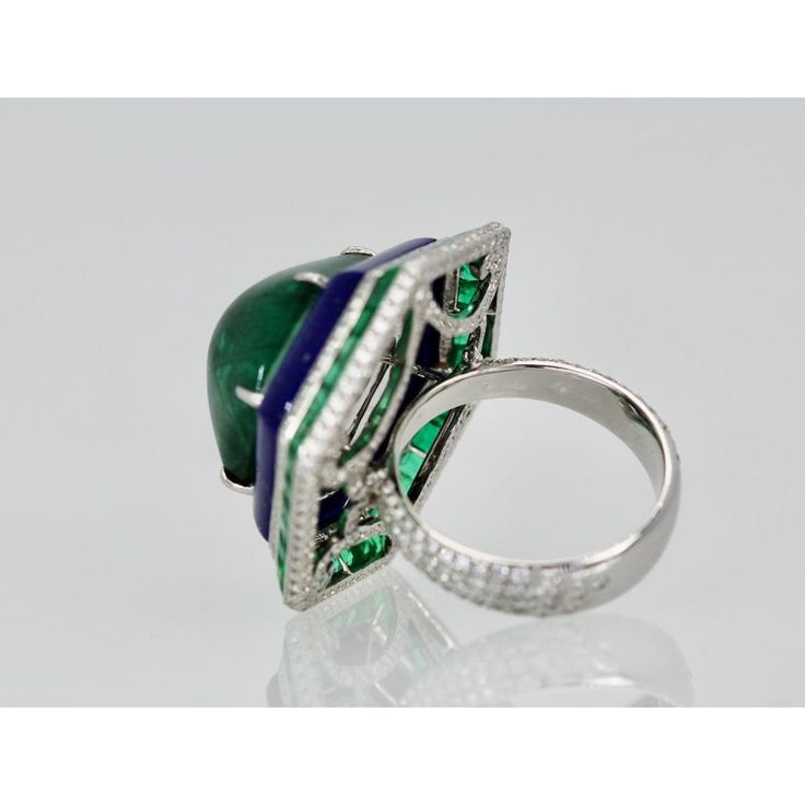 This is part of Chairish’s Fine Jewelry assortment.  Emerald Lapis Diamond Ring 18K  This modern Emerald Lapis and Diamond ring is absolutely exquisite and made in 18K white gold. There are 48 square Emeralds surrounding a Lapis band that circles this amazing 29 carat Sugarloaf Bullet Emerald. No details have been missed including the underside is set with Diamonds as are the shoulders of this setting. There are two rows of Diamonds above and below the the Emeralds Squares and the height of the Luxury 14k White Gold Green Diamond Ring, Luxury Green Diamond Ring In 14k White Gold, Luxury Emerald Rings With Polished Finish, Luxury Emerald Rings With Bezel Setting, Luxury Hallmarked Round Cut Emerald Ring, Luxury Emerald Rings Hallmarked, Luxury Platinum Halo Ring With Gemstone, Luxury Multi-stone Round Emerald Ring, Luxury Polished Emerald Ring