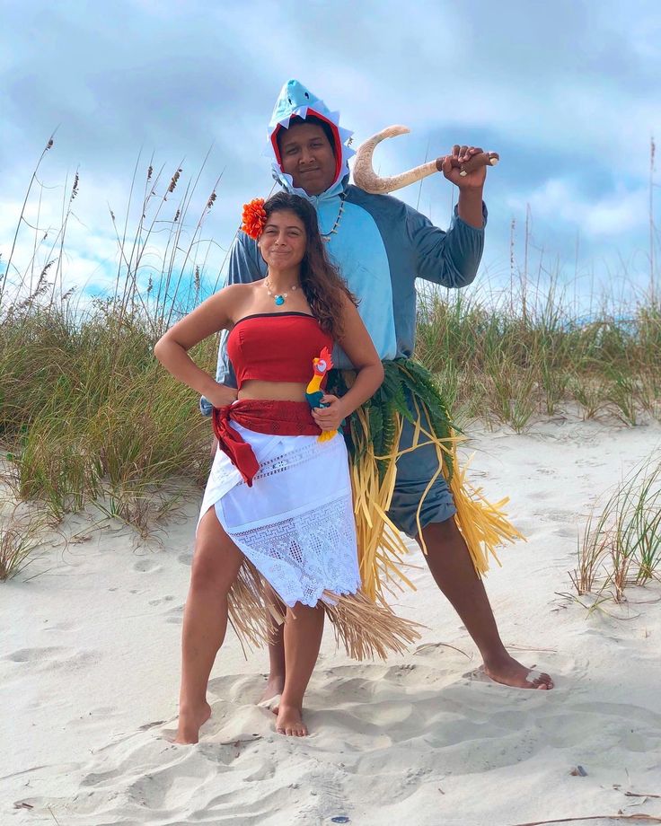 a man and woman dressed up in costumes on the beach, posing for a photo