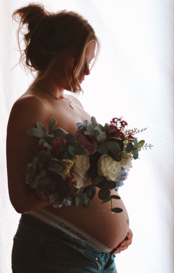 a pregnant woman with flowers on her belly holding a flower bouquet in front of her stomach