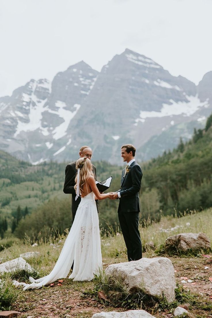 a bride and groom holding hands during their wedding ceremony at the top of a mountain