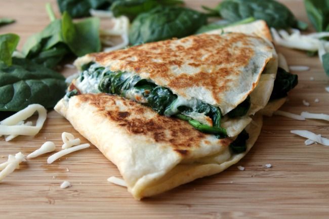 a cut in half sandwich sitting on top of a wooden cutting board next to spinach leaves