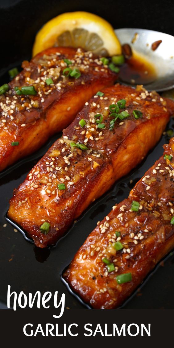 salmon fillets with sesame seeds and lemon wedges on a black plate next to a spoon