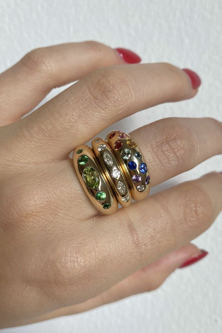 a woman's hand with three different colored stones on it and two gold rings