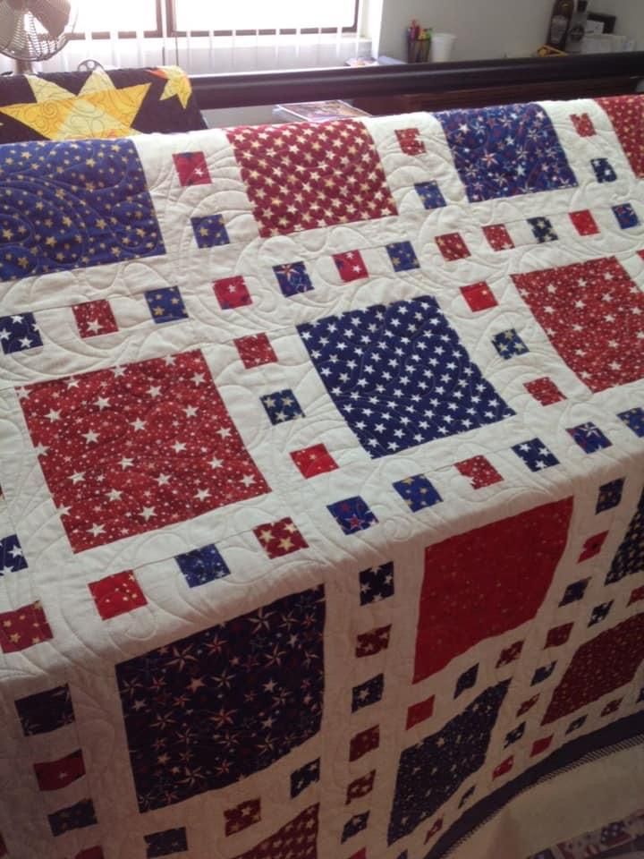 a red, white and blue quilt on a bed with a window in the background