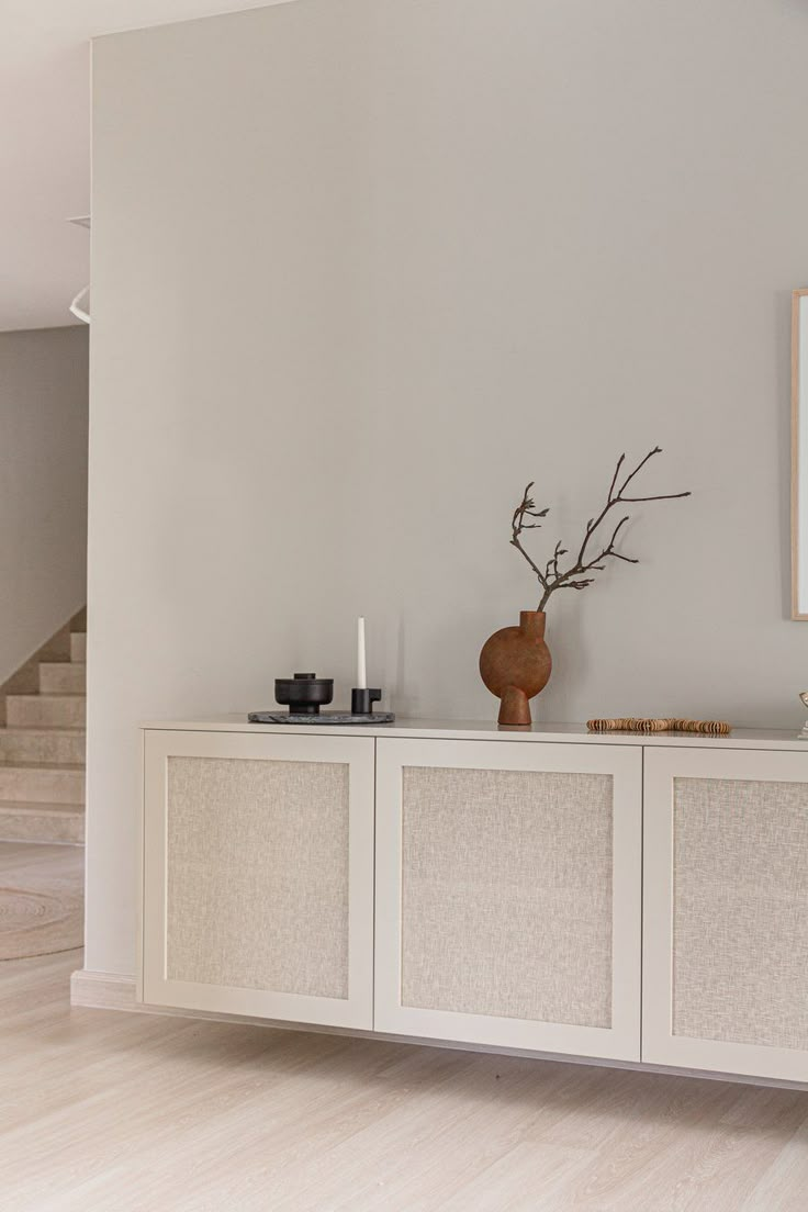 a white cabinet with some vases on top of it in a living room area