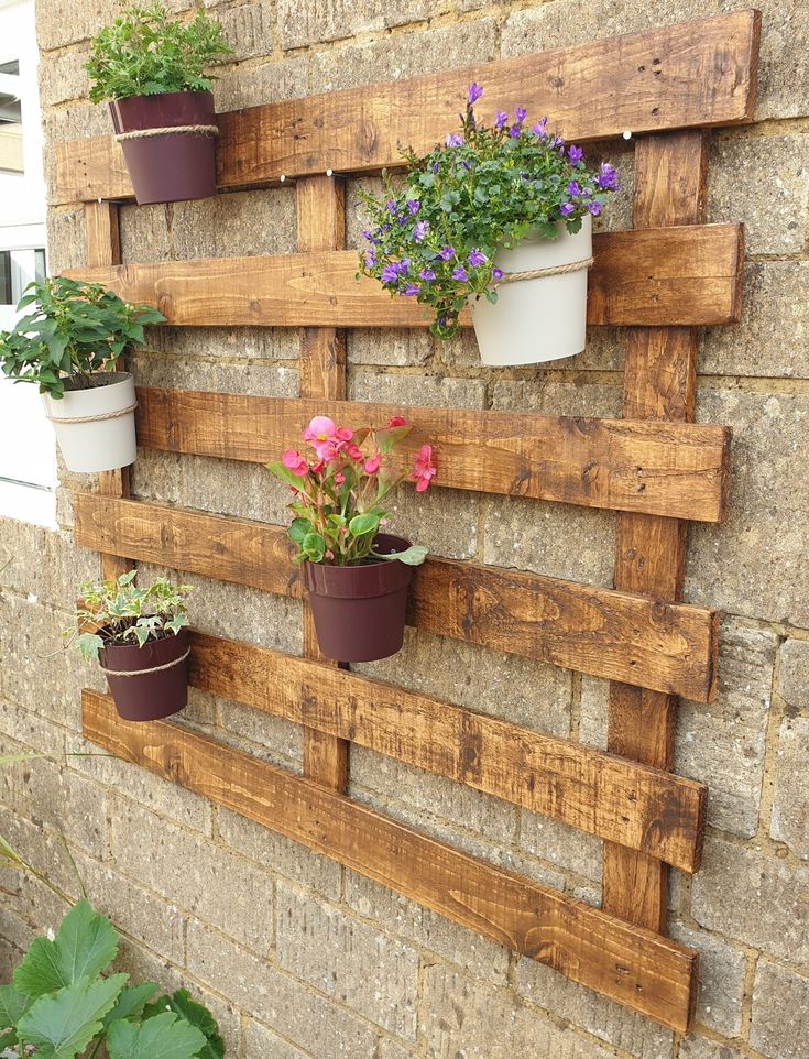 several potted plants are placed on a wooden pallet mounted to a brick wall